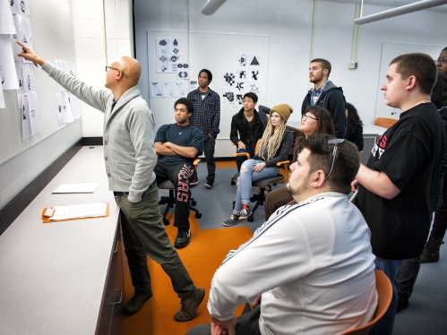 a male professor pointing out images on a wall to his college students