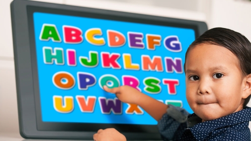 young boy pointing at a letter from the alphabet on a touchscreen while biting his lips. 