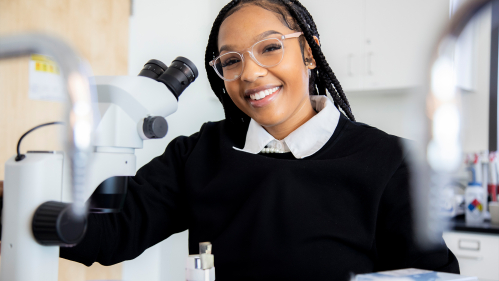 Chemistry student smiles at microscope.