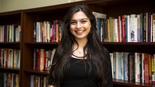 Student wearing a black blouse smiles in front of a row of bookcases