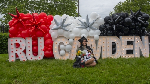 Commencement 2024 graduate sitting in front of ru camden sign