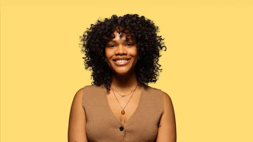 Headshot of student wearing a vest in front of a mustard backdrop