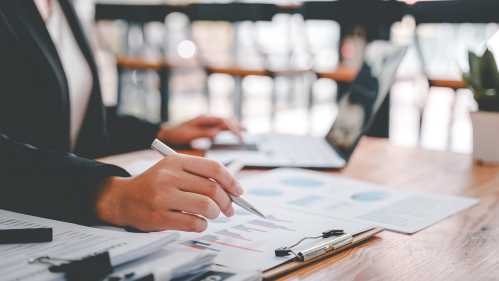 Person at desk with computer and multiple documents on clipboards
