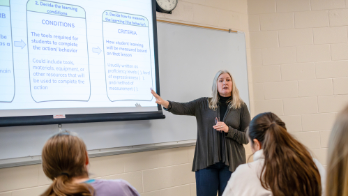 Professor in front of class showing learning conditions and criteria