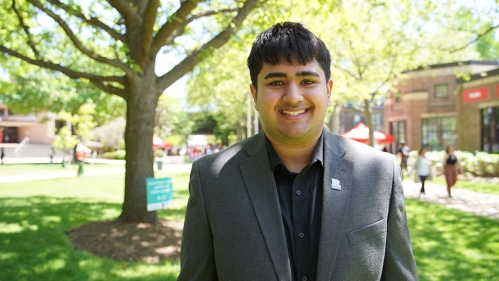Shaan Mody wears a gray suit standing on the campus quad