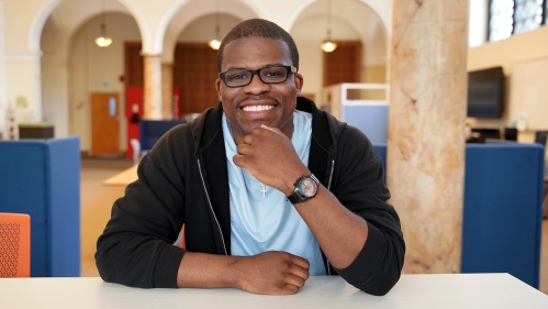 Alumnus leans against a table and smiles inside Digital Commons.