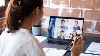 Female attending virtual conference call on laptop computer. The computer screen shows various individuals in the online meeting.