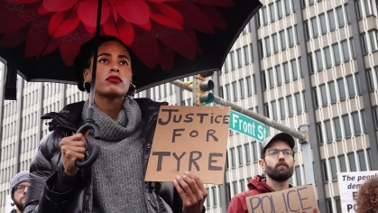 Protester under umbrella holding a "Justice for Tyre" sign