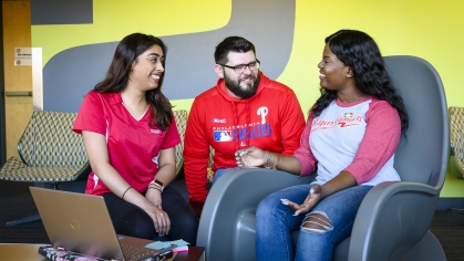 two female college students and one male college student sitting in a dorm lounge with an open laptop