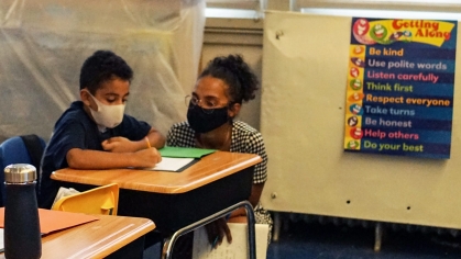 Elaysel Germán squatting down to help a young student with his homework