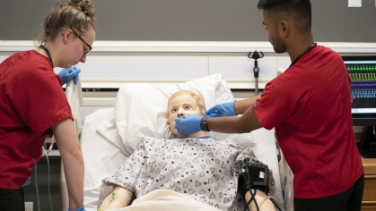 a female and male nursing student examining a dummy patient in a hospital bed