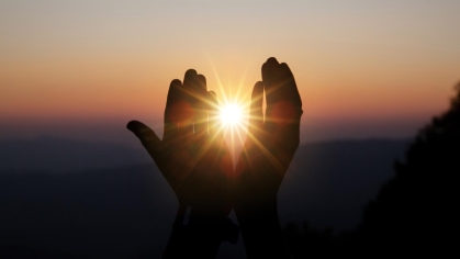 Spiritual prayer hands with sun shining in background as a beautiful sunset