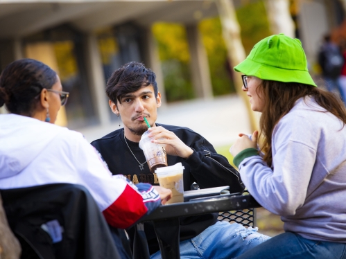 two female college students and one male college student drinking Starbucks coffee at an outside table