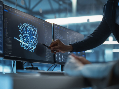  Downloaded With Screen Setup Showing AI Code and Model Visualization, Female Developer Works Closely with a Black Team Leader Standing Beside Her, Discussing Improvements and Refinements to Their AI System