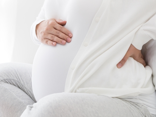 Photo of pregnant woman holding belly with hand on back of spine