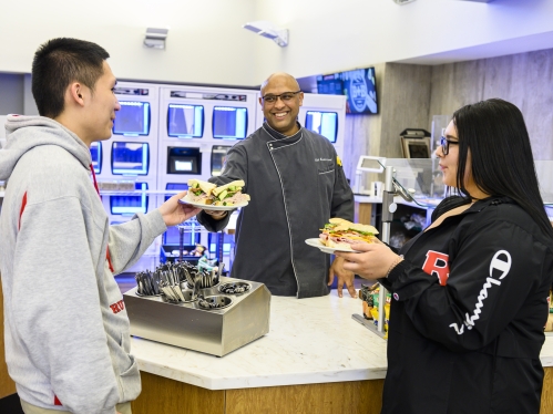 one male and one female college student being served food by a male staff member in the Rutgers–Camden dining hall