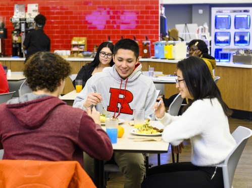 male and female Rutgers–Camden students sitting at a table, eating in a dining hall