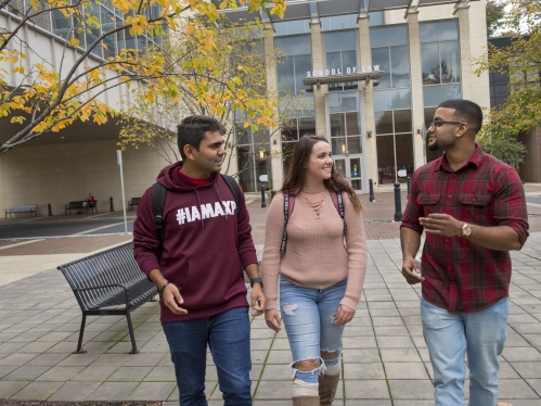 two male college students and one female college student walking in front of the Rutgers' School of Law building