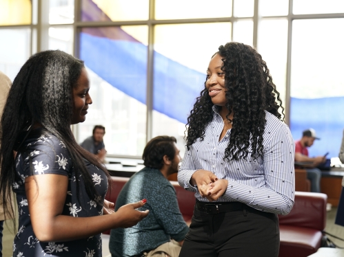 two female law students standing and talking with other college students in the background