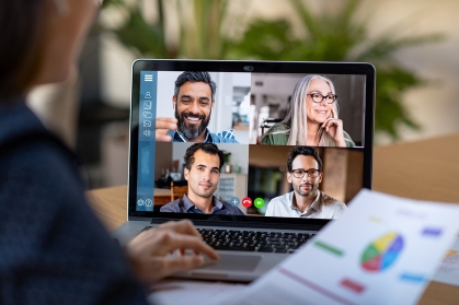 Business person attending virtual conference meeting on laptop. The laptop screen shows the four participants in the conference.