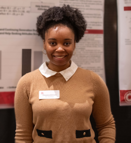 Student with tan shirt smiles in front of her research poster