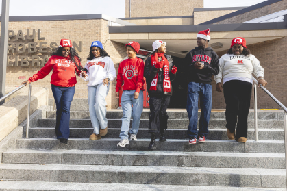 Students wear crocheted Rutgers hats and a scarf on the Robeson Library steps. 
