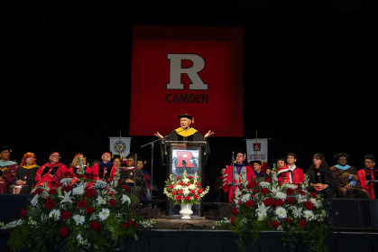 Admiral William J. Fallon speaks behind podium with the read Rutgers R in the background 