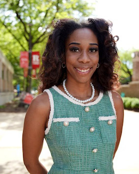 Student in green dress smiles outside with Rutgers banner in the background