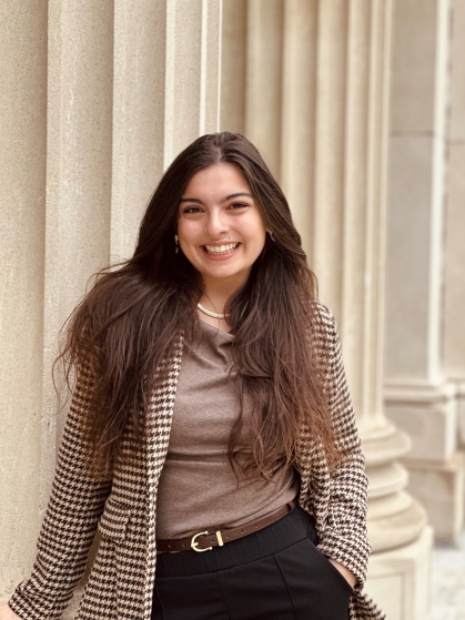 Student wearing a houndstooth jacket stands in front of Digital Studies Center pillars