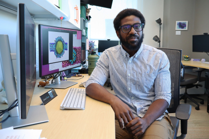 Student leans against a desk with two monitors