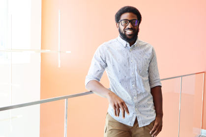 Student smiles and stands in front of an orange wall and chandelier