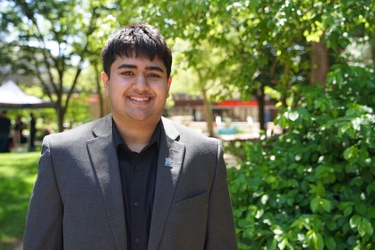 Shaan Mody wearing a gray suit smiles outside on the campus quad