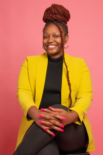 A smiling Nyree Oliver sits wearing a gold jacket. 