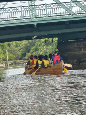 Honors College Impact Day Boat Trip: Students rowing down river passing under a bridge