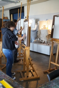 Art student standing in front of easel working on a charcoal class activity