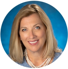 Amy Mansue, the Commencement Speaker for the School of Nursing is pictured smiling in front of a blue background wearing a blue checked blouse.